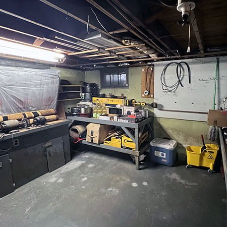 Dimly lit basement showing a workbench with various tools and and unfinished ceiling above