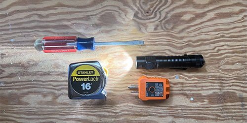 Flathead screwdriver, flashlight, tape measure, and basic receptacle tester on a wooden workbench